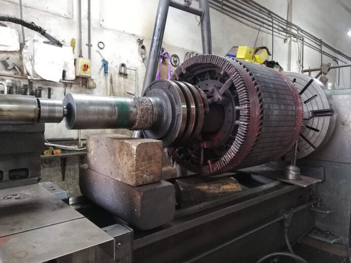 Electric motor rotor mounted on lathe for reconditioning